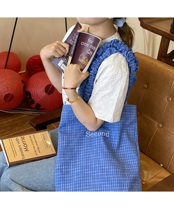 Dettaglio borsa tote in tela a quadri blu con tracolla a balze e ricamo decorativo