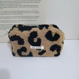 Detail of leopard print plush makeup bag featuring a May Rabbit woven label and zipper