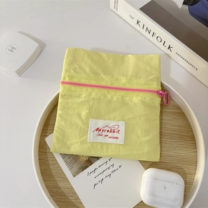 Flat lay of a yellow canvas pouch with pink zipper on a white tray with lifestyle items