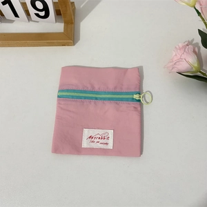 Macro detail of compact pink nylon coin purse with contrast green zipper and logo label