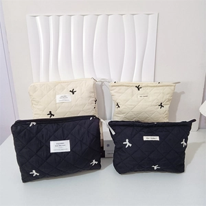 Detailed view of quilted makeup bags in cream and black with delicate bow embroidery