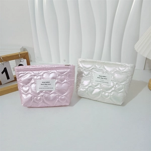 Close-up of heart-quilted PU leather cosmetic bags in pink and white with metal zippers