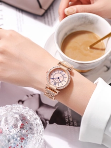 Détail d'une montre en or rose avec strass, chiffres romains et bracelet métal au poignet