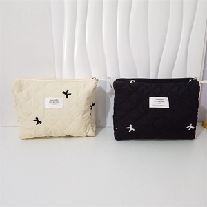 Detail of cream and black quilted cosmetic bags with bow embroidery and metal zipper
