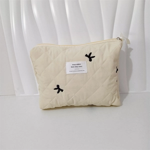 Close-up of quilted cosmetic bag featuring black bow embroidery and metal zipper