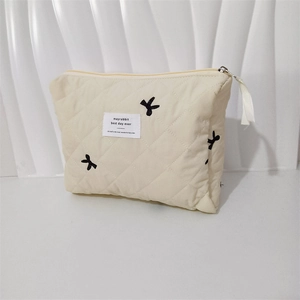 Close-up of quilted cream makeup bag with rabbit embroidery and ribbon zipper pull