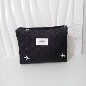 Close-up of black quilted makeup bag featuring white bow embroidery and metal zipper
