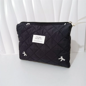 Detail of black quilted makeup bag featuring white bow embroidery and zip closure