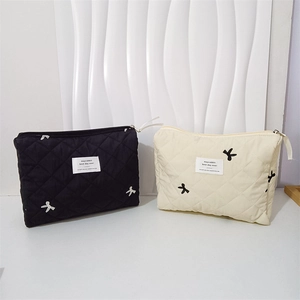 Detail of quilted cosmetic bags with bow embroidery in black and cream colors