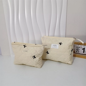 Set of two cream quilted cosmetic bags with black bow embroidery and metal zipper