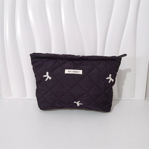 Detailed view of black quilted cosmetic bag featuring white bow embroidery and top zipper