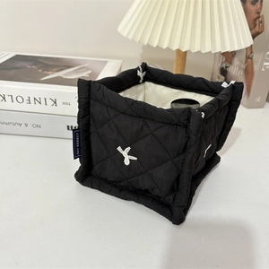 Close-up of black quilted storage basket with white embroidery on a minimalist desktop