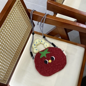 Detail of red plush tomato bag with embroidered eyes and woven rope shoulder strap