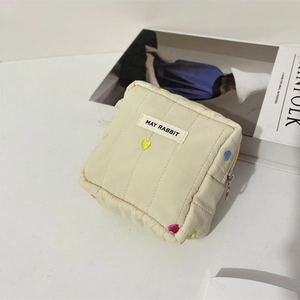 Detailed view of beige quilted makeup bag with colorful heart embroidery and brand label