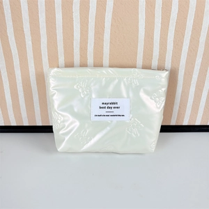 Detail view of cream white quilted makeup bag with embossed bow patterns and zipper