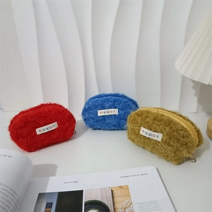 Tre mini trousse in peluche a forma di conchiglia in rosso, blu e giallo su tavolo bianco