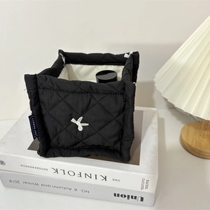 Detailed close-up of quilted black storage basket with white embroidery on art books