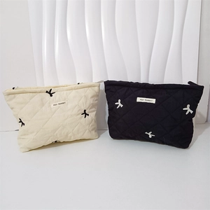 Close-up of quilted cosmetic bags with bow embroidery in black and cream colors