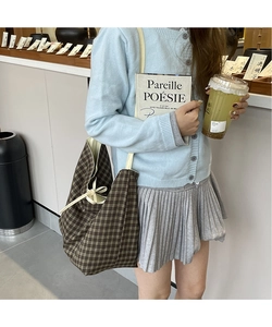 Detail of a large brown plaid tote bag with decorative side bow in a cafe setting