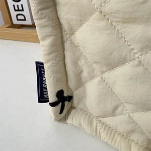 Detail of beige quilted fabric storage basket with embroidery and brand woven label