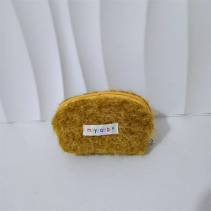 Dettaglio del portamonete in peluche giallo zenzero con texture morbida e etichetta bianca