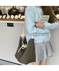 Close-up of brown plaid canvas tote bag with beige bow ribbon detail in a cafe setting