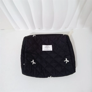 Detail of black quilted cosmetic bag featuring white bow embroidery and logo patch