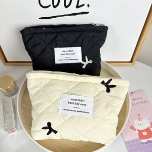 Close-up of quilted cosmetic bags in black and cream with bow embroidery and zip closure