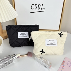 Close-up of quilted cosmetic bags with bow embroidery in black and beige finishes