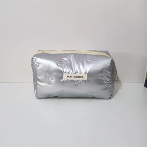 Detail of silver quilted makeup bag with embossed bow patterns and fabric label