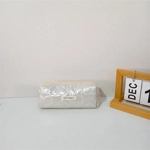 Detail of heart-quilted white pencil case with brand label and golden zipper closure