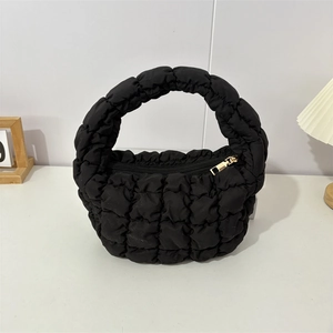 Detail of black puffy quilted handbag featuring shiny nylon fabric and gold metal zipper
