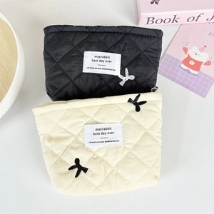 Close-up of quilted cosmetic bags in black and beige with bow embroidery and logo label
