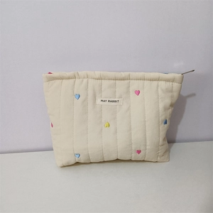 Close-up of quilted cream cosmetic bag with colorful heart embroidery and fabric label