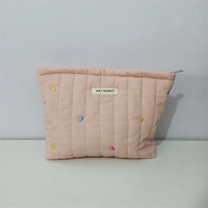 Close-up of quilted heart embroidery and branded label on pink cosmetic pouch