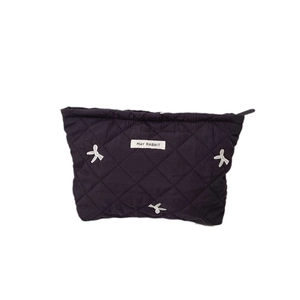 Quilted makeup bag with white bow embroidery and brand label on dark fabric