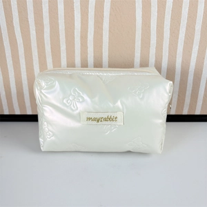 Close-up of pearl white PU quilted cosmetic bag with embossed bow patterns and zipper