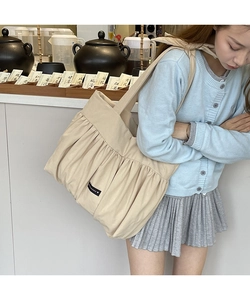 Detail view of the beige canvas tote bag with pleated fabric and small brand label