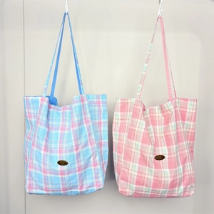 Detail of checkered canvas tote bag featuring a stitched leather Handmade logo tag