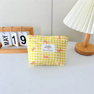 Detail of yellow checkered canvas makeup bag with floral bow print on white desk