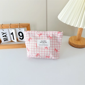 Detail of pink plaid canvas cosmetic bag with bow patterns and silver zipper on white desk