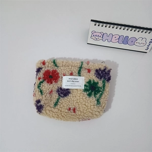 Flat lay of cream fleece makeup bag with colorful floral embroidery and white woven label