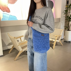 Détail du sac seau bleu en peluche avec texture frisée en fausse fourrure et étiquette cuir