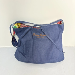 Close-up of denim tote bag featuring orange embroidery and colorful ethnic pattern lining