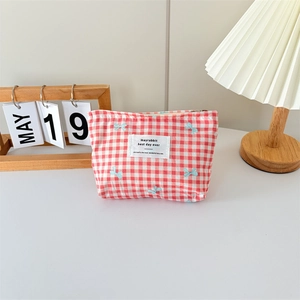 Close-up of red plaid canvas makeup bag with blue bows and soft lighting background