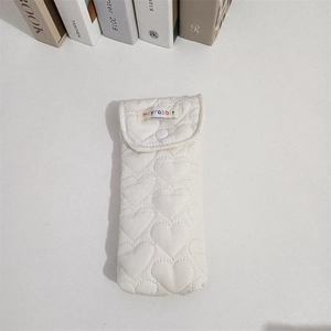 Detail view of cream quilted heart pattern fabric case with button closure and brand label