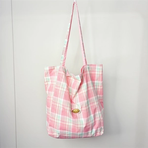 Detail of a pink and green plaid tote bag with a gold handmade label on fabric