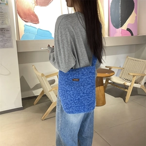 Détail du sac bandoulière bleu en peluche avec étiquette en cuir et texture de fourrure
