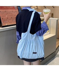 Detail of light blue pleated tote bag with Romance text on the front carried by a model