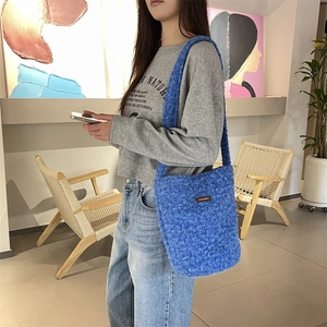 Détail du sac seau bleu en peluche avec texture douce et écusson logo marron sur le devant